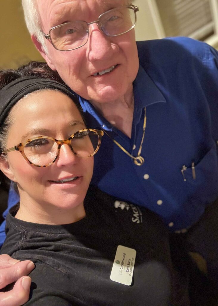 A Castlewood team member shares a joyful moment with a senior resident, both smiling warmly while celebrating meaningful connections in the community.