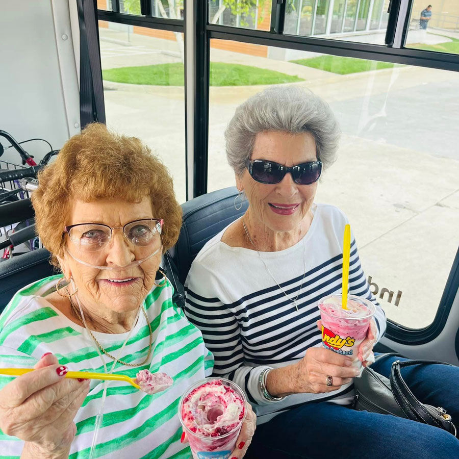 Two senior living community residents sitting on a bus, smiling, and enjoying frozen custard from Andy's.