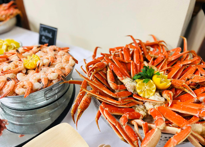 Seafood spread featuring a chilled bucket of shrimp and a large platter of crab legs, garnished with fresh lemon slices and parsley, ready to be served for a seafood buffet.