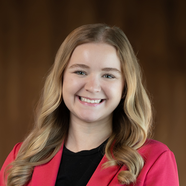 Nikki Walters, Resident Services Director at The Castlewood Senior Living, smiling brightly with long blonde curls, wearing a black top and a vibrant red blazer.
