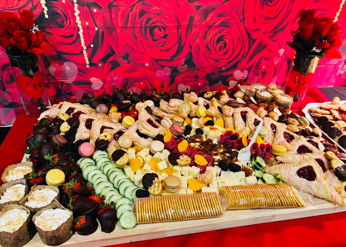 Valentine-themed charcuterie board featuring crackers, cheeses, cucumber, macarons, chocolate-dipped strawberries, and a standout pairing of goat cheese and bacon jam.