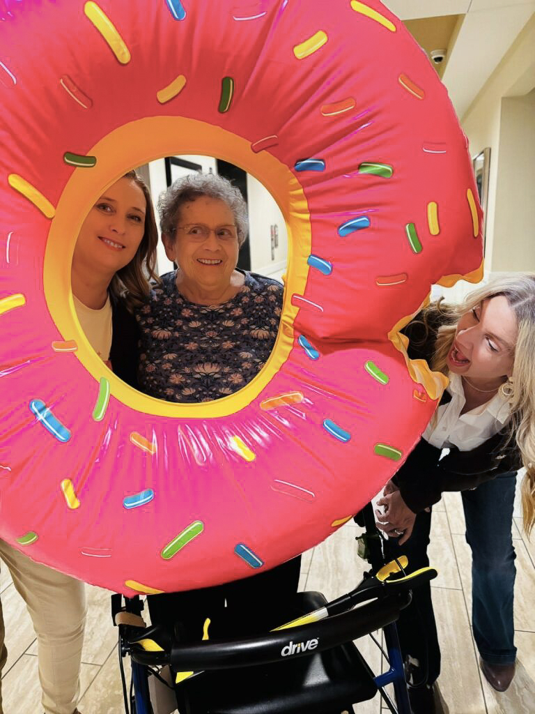 Team members and resident posing playfully with a large, inflatable pink donut during an event.