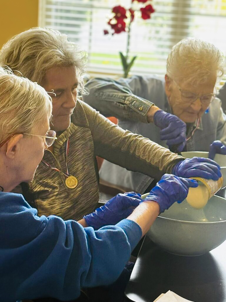 Residents, wearing blue food-safe gloves, work together on a baking project.