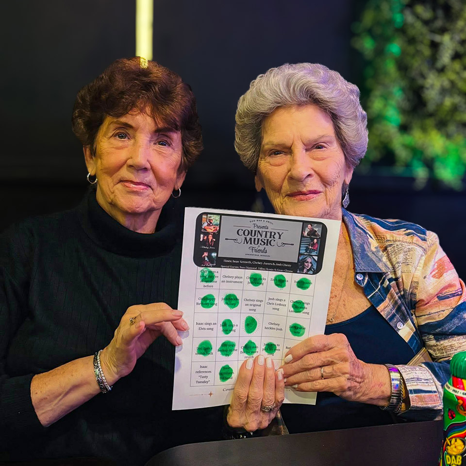 Two women hold up a flyer from a community event, smiling together.