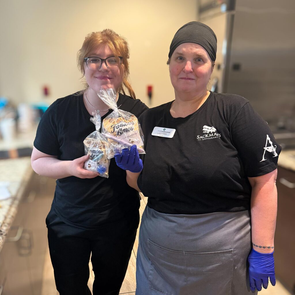 Two team members at The Castlewood Senior Living smile, holding wrapped treats.