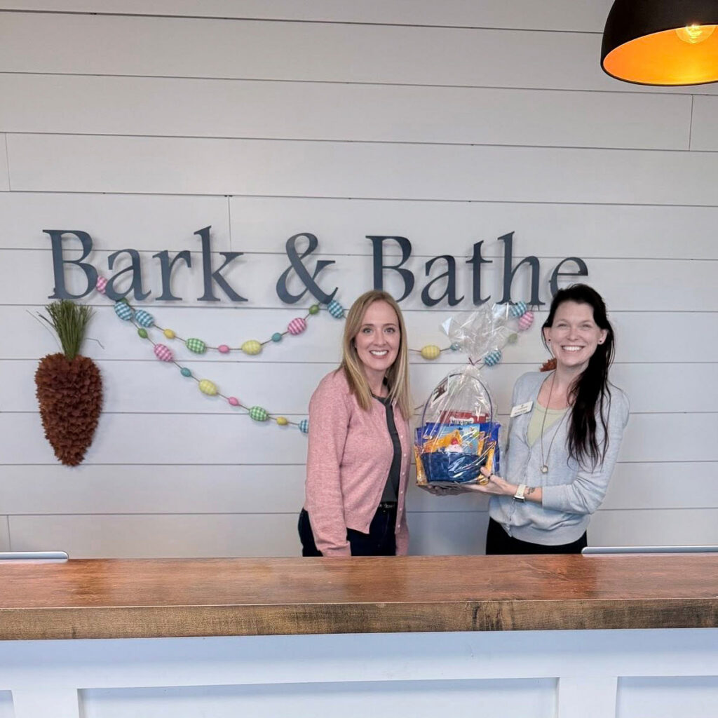 A team member from The Castlewood Senior Living presents a gift basket to the smiling owner of Bark & Bathe.